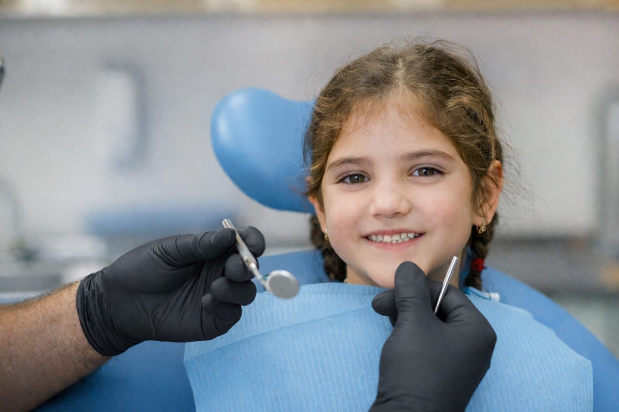 Zahnärztliche Untersuchung bei einem Kind: Ein Mädchen sitzt im Behandlungsstuhl, während mit Spiegel und Instrumenten die Zähne geprüft werden.