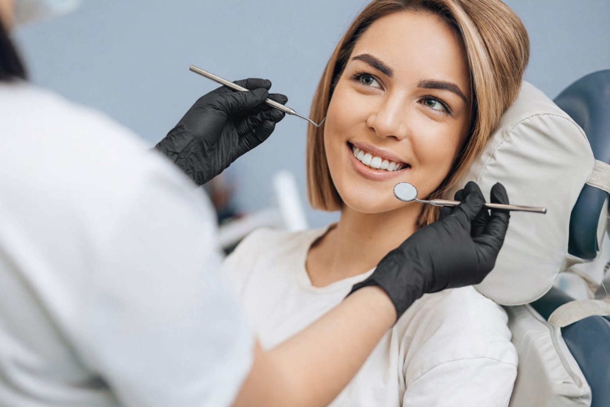 Junge Frau bei Zahnkontrolle: Eine Patientin sitzt im Stuhl, während der Zahnarzt mit Instrumenten eine Untersuchung durchführt.